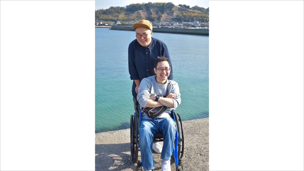 海で観光している木村さんと木村さんの車椅子を押す久保田さん