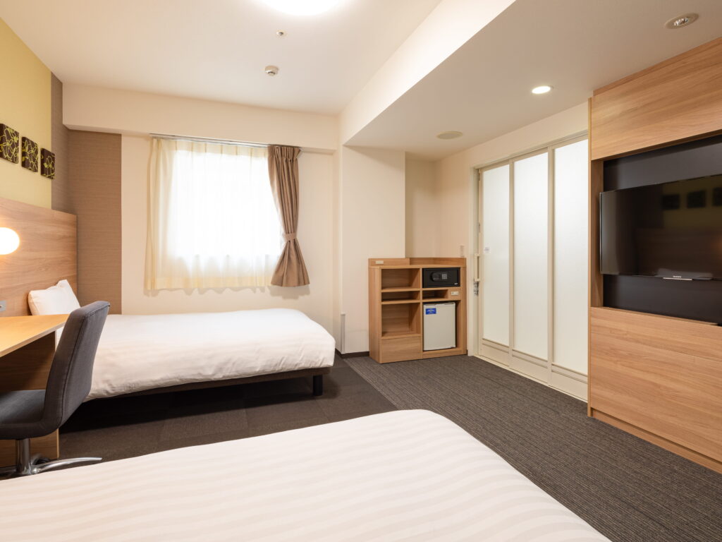 コンフォートホテル、ユニバーサルルームの室内の写真。左側に2台のベッド、その間に机と椅子がある。右手にはテレビとユニットバスがある。