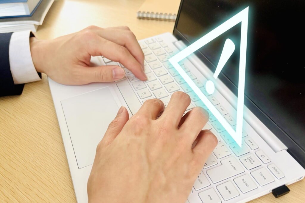 パソコンを操作する手と警告マーク